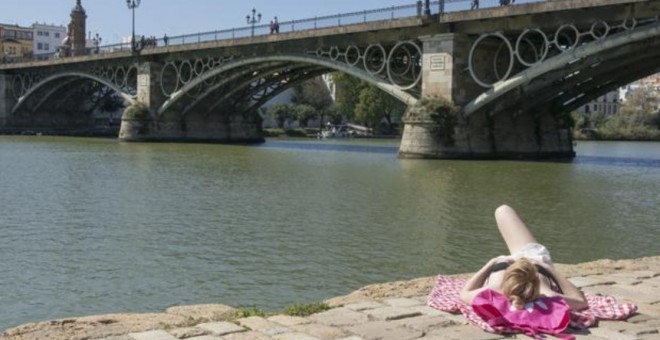 Una mujer toma el sol a orillas del Guadalquivir, bajo el Puente de Triana en Sevilla / EFE (RAÚL CARO)