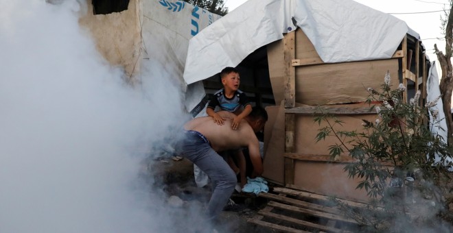 Un migrante coge a un niño mientras huyen de gases lacrimógenos disparados por la policía antidisturbios durante una manifestación, después de un incendio en el campamento de Moria en la isla de Lesbos. REUTERS/Giorgos Moutafis