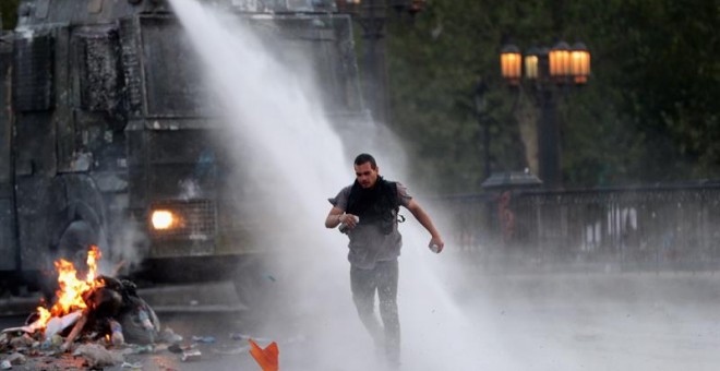 Un manifestante huye del chorro de agua lanzado por la policía durante una nueva jornada de protestas contra el Gobierno del presidente chileno Eduardo Piñera este sábado, en Santiago (Chile). El alza en el precio del pasaje del metro de Santiago prendió