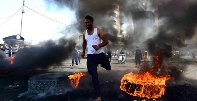 Un manifestante corre entre rueda de coche ardiendo durante una manifestación en la plaza de Khillani en Bagdad, Irak.EFE/ Murtaja Lateef