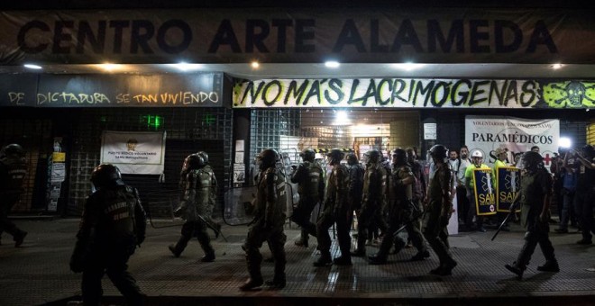 Un grupo de Fuerzas Especiales de Carabineros camina frente al cine Arte Alameda custodiado por voluntarios sanitarios el pasado viernes 13 de diciembre. /EFE