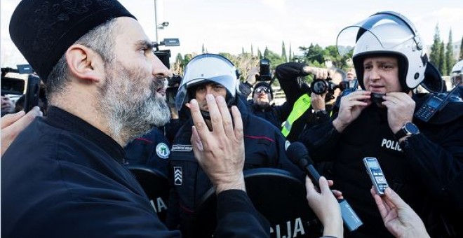 Un sacerdote de la Iglesia Ortodoxa Serbia habla con un policía antidisturbios en un puente cerca del parlamento, antes de votar un proyecto de ley sobre 'Libertades religiosas y derechos legales de las organizaciones religiosas' en Podgorica | Reuters
