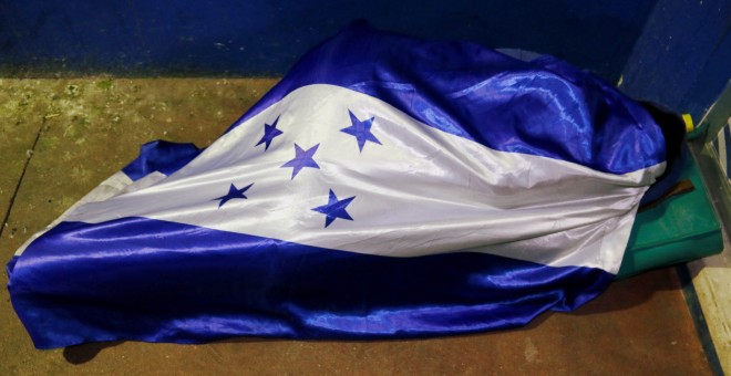 Uno de los migrantes durmiendo arropado por la bandera de Honduras. / Reuters