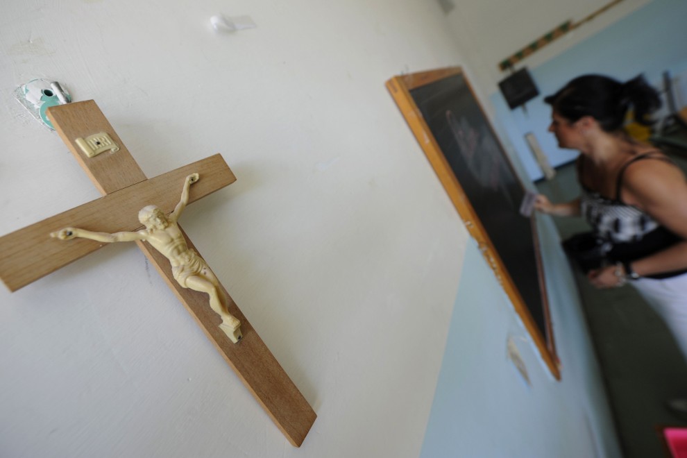 Un crucifijo cuelga en la pared de un aula en el que una profesora escribe en la pizarra. AFP