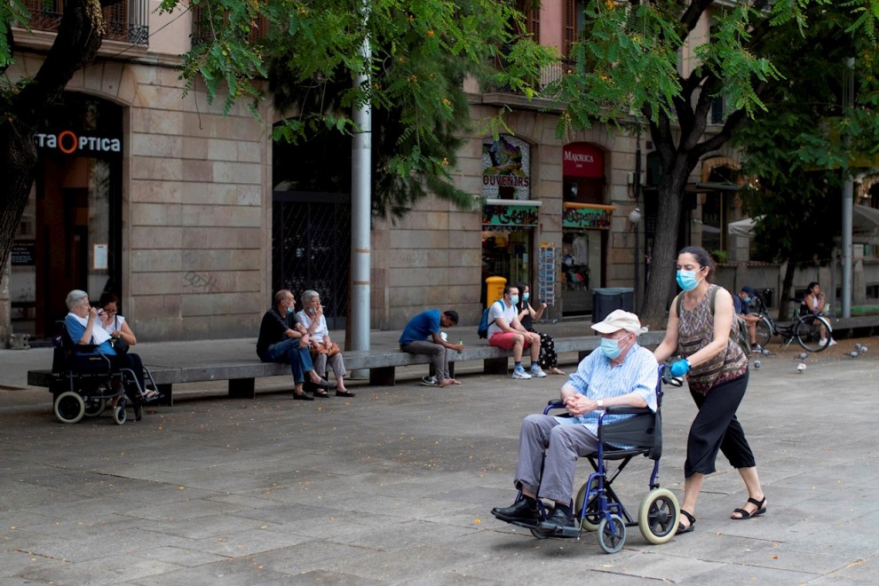 Una mujer empuja la silla de un anciano en el centro de Barcelona.  - EFE