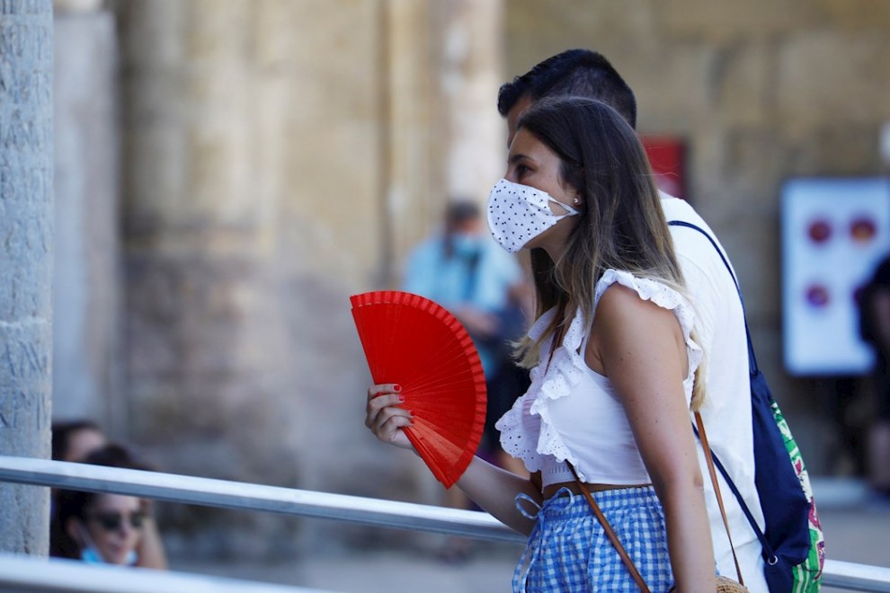Una mujer protegida con unas mascarilla mientras se abanica para aliviar las altas temperaturas de este jueves en Córdoba. | EFE