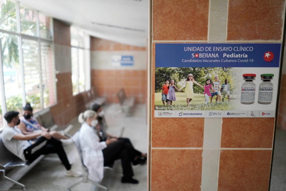 Imagen de archivo de varias personas sentadas cerca de un cartel que anuncia los ensayos clínicos de la vacuna Soberana 02, en una clínica sanitaria en La Habana. - REUTERS