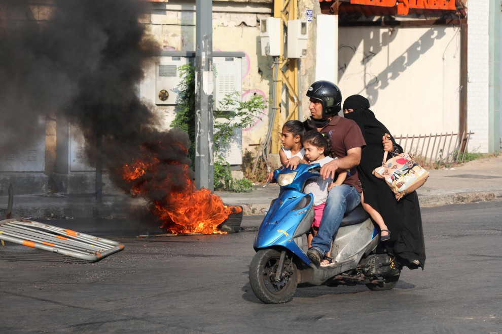 Una familia ocupa una moto mientras arden neumáticos cerca con motivo de las protestas por la explosión del año pasado ocurrida en el puerto, en Beirut. - REUTERS