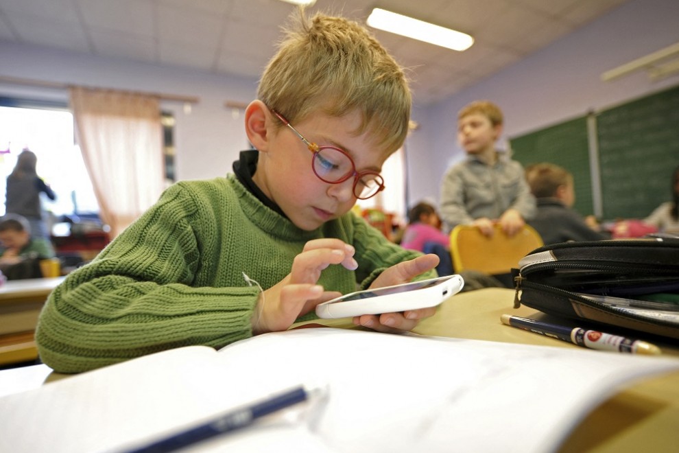 Un niño comprueba un dispositivo móvil durante una clase en un colegio.