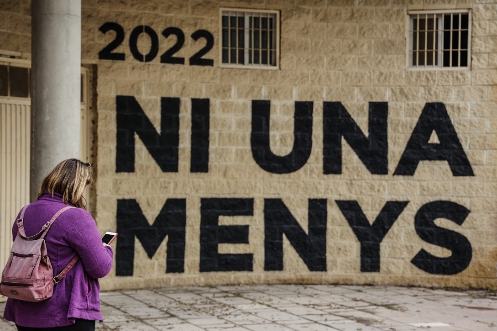 Una mujer pasa por delante de una pared donde se puede leer 'Ni una menos' en un acto en memoria de las víctimas de violencia de género y sus hijas e hijos, en el antiguo cauce del Turia, a 8 de marzo de 2022, en Valencia, Comunidad Valenciana