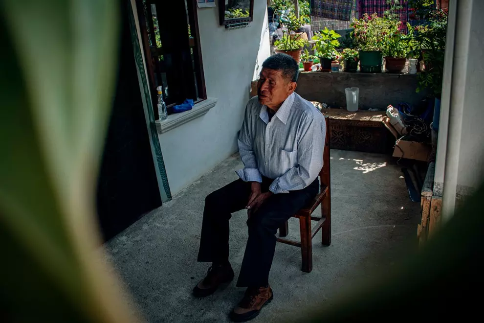 Román Coc sentado en una silla de madera en el patio que separa la cocina comedor de las habitaciones.