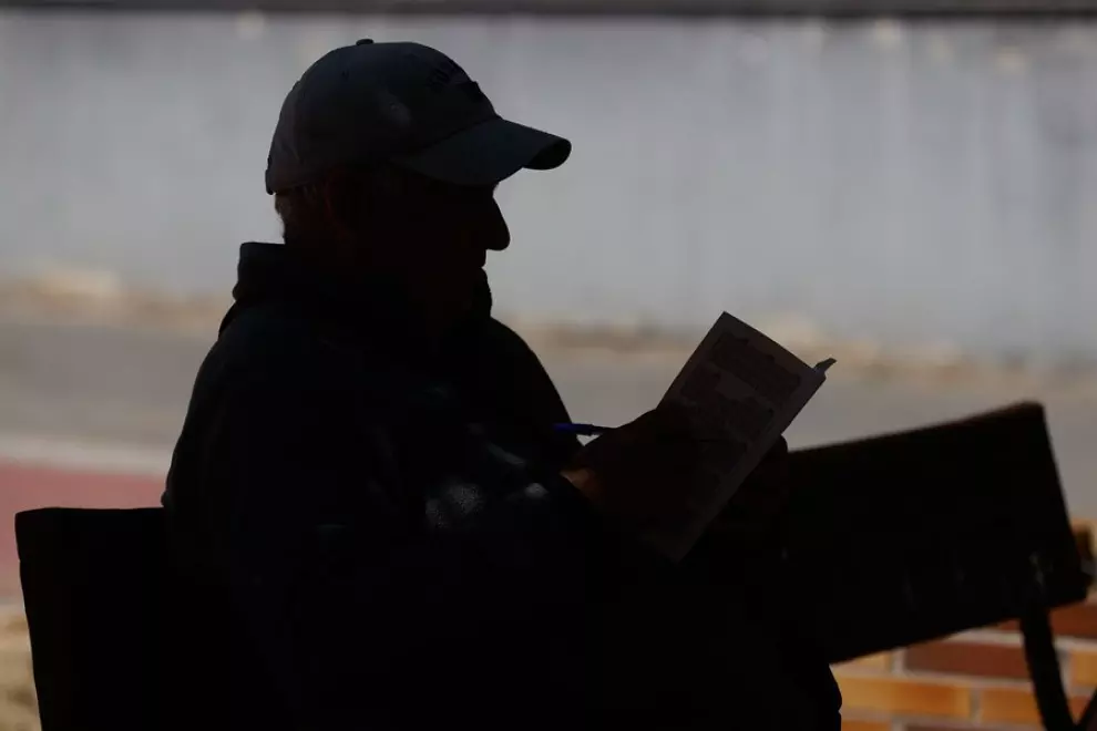 Un anciano lee un libro en un banco de un parque en Madrid.