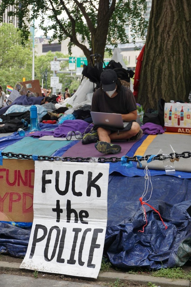 Un participante en el Occupy City Hall de Nueva York sostiene un ordenador Apple detrás de una pancarta que reza "que se joda la Policía". SARAH YÁÑEZ-RICHARDS