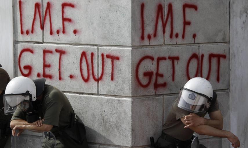 Un par de policías antidisturbios descansan junto a una pintada contra el FMI, durante una manifestación contra las medidas de austeridad (5 de mayo de 2010). REUTERS/Yorgos Karahalis