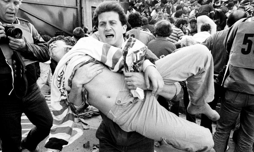 Un aficionado traslada a uno de los heridos en la avalancha en el estadio Heysel de Bruselas, en la final de la copa de Europa entre  la Juventus y el Liverpool, que provoó la muerte de 39 personas y 600 heridos (29 de mayo de 1985). REUTERS/Nick Didlick