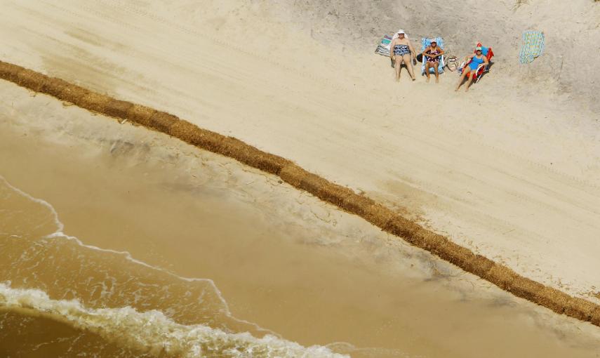 Unos bañistas toman el sol detrás de un muro de balas de heno, colocadas para absorber el petróloe de la marea negra provocada por el accidente de una plataforma de BP en el Golfo de México (11 de mayo de 2010). REUTERS / Brian Snyder