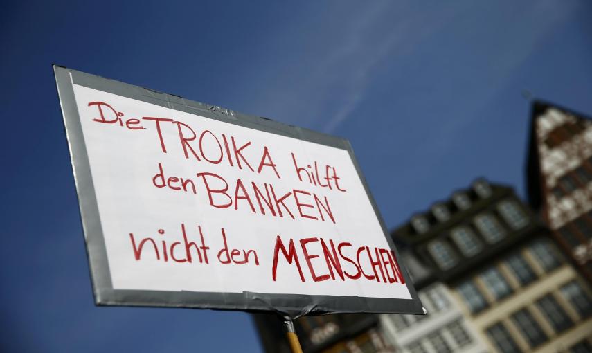 Una pancarta que dice, en alemán, "La Troika ayuda a los bancos y no a las personas", durante la concentración contra la austeridad en la UE celebrada en la plaza del Ayuntamiento, en el centro histórico de Fráncfort, tras la inauguración de la nueva sede