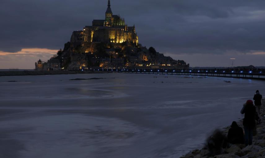 La gente se sienta en un terraplén para observar como la marea  rodea la abadía de Mont Saint-Michel, del siglo XI,en Normandía. REUTERS / Pascal Rossignol