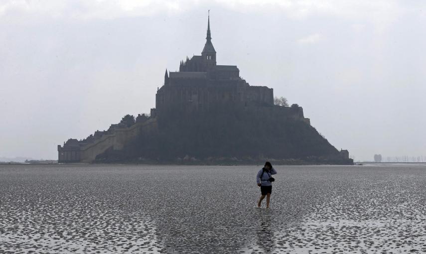 Una mujer camina en la arena durante la marea baja cerca de la abadía del Mont Saint-Michel, en Normandía. REUTERS / Pascal Rossignol
