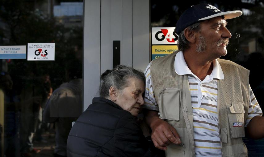 Vallia (L), un jubilado de 75 años de edad, de Atenas, se aferra a la puerta de una sucursal del Banco Nacional de Grecia con la esperanza de obtener su pensión, junto a otros jubilados en Atenas, tras establecerse el control de capitales en el país por l