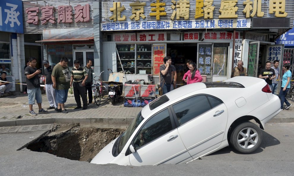 Transeúntes echan un vistazo a un coche que ha caído parcialmente en un socavón por una calle de Beijing. REUTERS