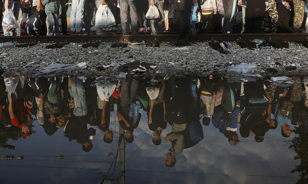 Refugiados sirios se reflejan en un charco mientras esperan en la frontera entre Grecia y Macedonia. REUTERS