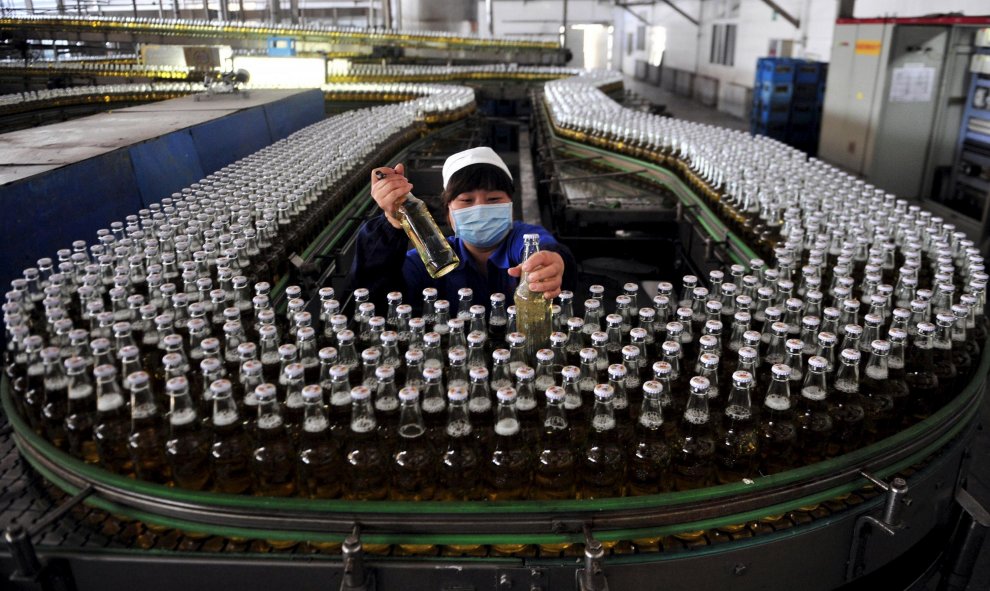 Una mujer recoge botellas de cerveza en una cadena de montaje dentro de una fábrica en Shenyang. REUTERS