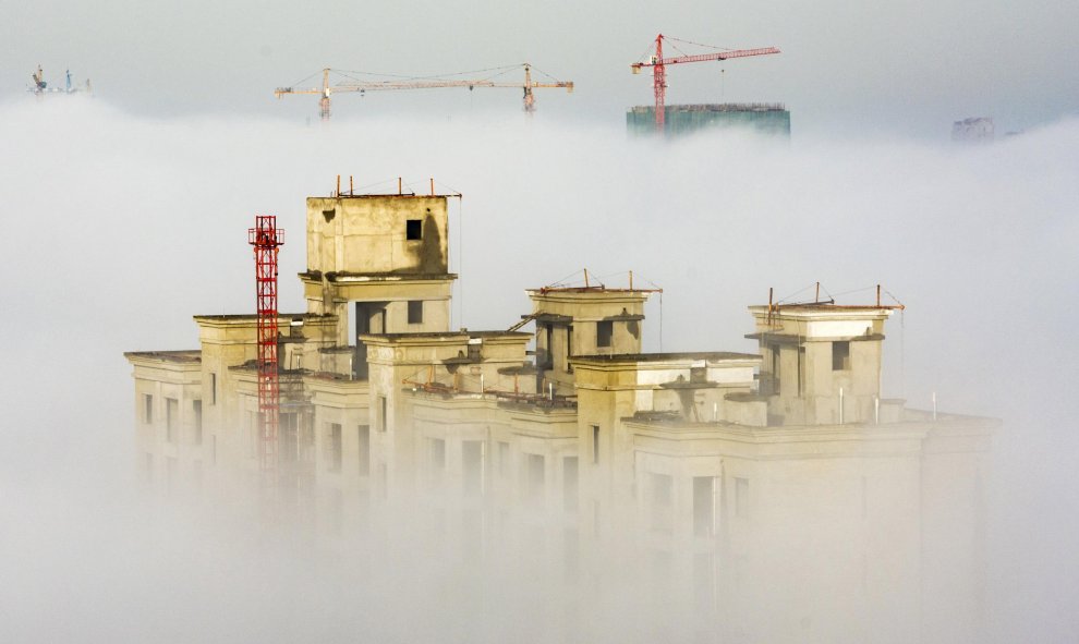 Grúas y edificios residenciales en construcción se ven entre una espesa niebla en Anyang, China. REUTERS/Stringer