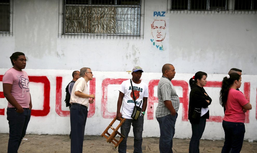 Un grupo de votantes espera su turno ante un graffiti de Hugo Chavez donde se lee "Paz. Vive". REUTERS/Nacho Doce