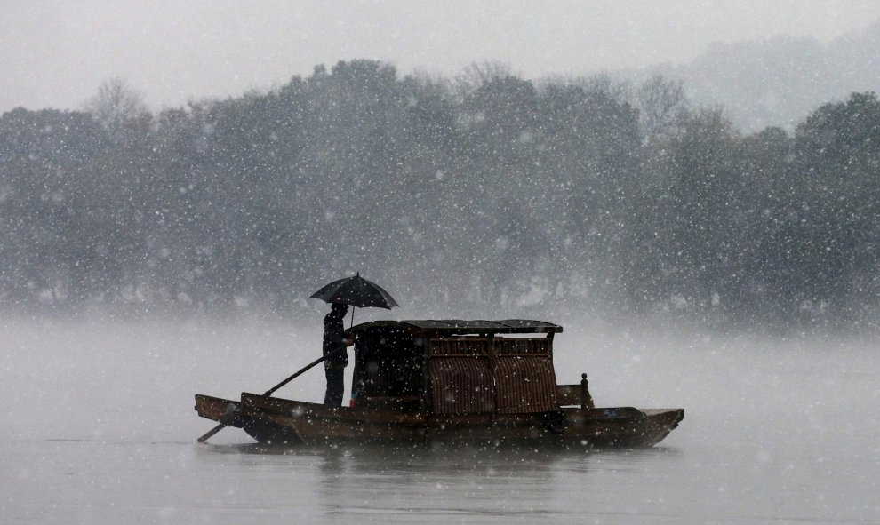 Un hombre agarra un paraguas para cubrirse de la nieve, mientras que ata un bote en el este del Lago de la provincia de Zhejiang, China. REUTERS/Stringer