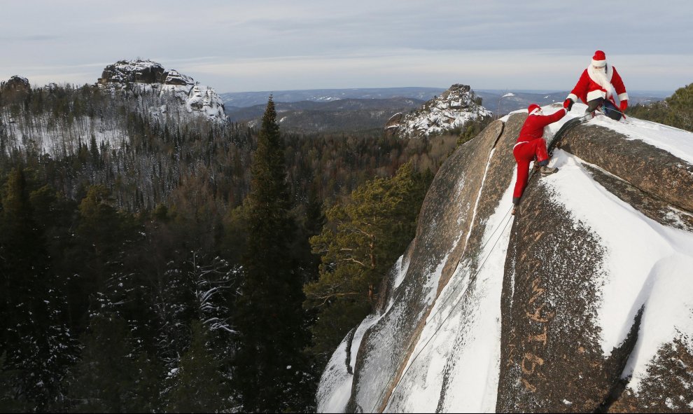 Un miembro de 'Sibspas', grupo de búsqueda y rescate siberiano, vestido de Papá Noel, le a la mano a su compañero que está disfrazado del Padre Invierno, mientras escalan la roca del 'Cuarto Pilar' en la Reserva Nacional de la Naturaleza de Stolby. Krasno