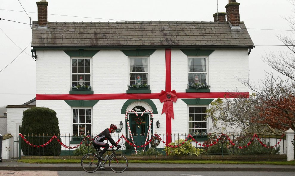 Un hombre montado en una bicicleta pasa por una casa decorada con regalos de Navidad. Norte de Bretaña. REUTERS/Phil Noble