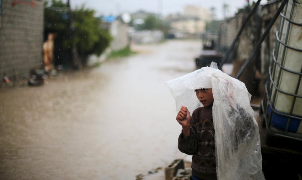 Un niño palestino se cubre la cabeza con una lámina de plástico en un día lluvioso en Khan Younis, al sur de la Franja de Gaza. REUTERS/Ibraheem Abu Mustafa