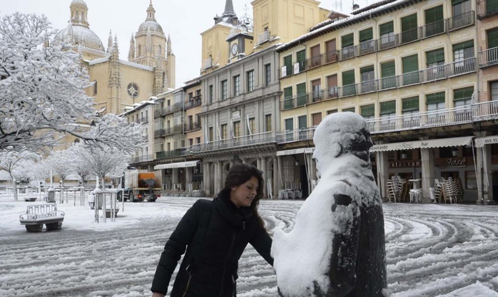 Una mujer retira la nieve sobre la escultura del poeta Antonio Machado, en la Plaza Mayor de Segovia, que despertó hoy con una capa de más de diez centímetros de nieve. EFE/Aurelio Martín