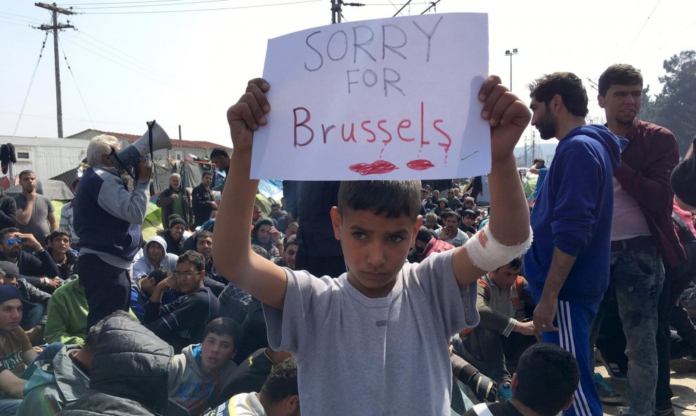 Un niño refugiado sostiene un cartel mientras refugiados y migrantes participar en una protesta contra el cierre de la frontera entre Grecia y Macedonia. REUTERS/Fedja Grulovic