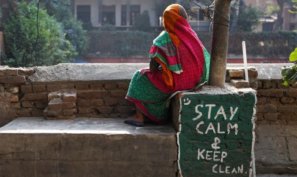 Una mujer nepalesa descansa sentada junto a una pintada con el mensaje "Permanece tranquilo y limpio" mientras siguen las obras de reconstrucción de un grifo de agua potable comunitario que resultó dañado en el terremoto, en Katmandú, Nepal. El país celeb