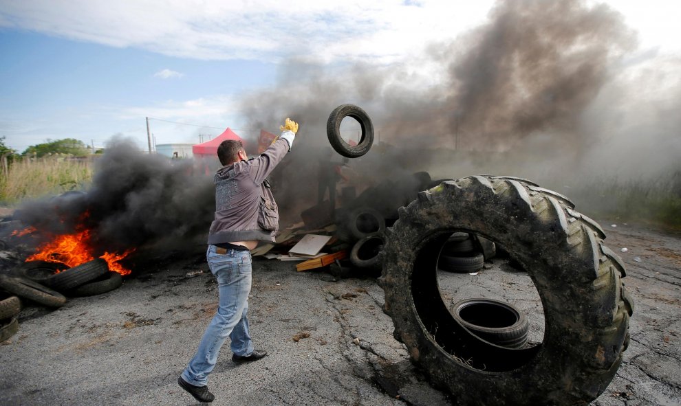 Un manifestante empleado de una petrolera lanza de un neumático sobre una barricada en llamas para bloquear la entrada del depósito.- REUTERS / Stephane Mahe / Foto