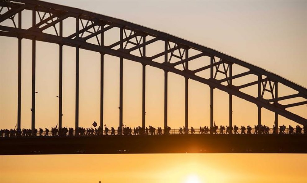 Varias personas cruzan un puente sobre el río Waal durante el primer día de la 100 edición de la Cuádruple Marcha Internacional de Nimega, Holanda. Este evento anual, que se celebra desde 1909, reúne a numerosos participantes que realizan marchas diarias