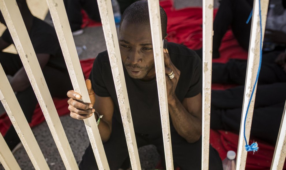 Un joven de senegal llama por teléfono en el muelle del puerto de Algeciras, donde ha pasado dos noches por falta de espacio en dependencias policiales y polideportivos. JAIRO VARGAS