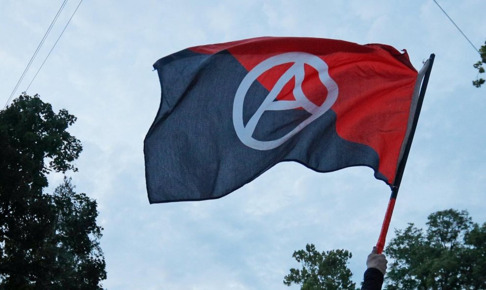 Un manifestante encapuchado ondea la bandera anarquista | REUTERS