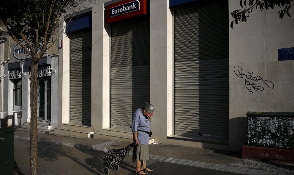 Una mujer con un carrito de la compra frente a una sucursal de Eurobank cerrada en Atenas, en una imagen de archivo. REUTERS / ALKIS KONSTANTINIDIS