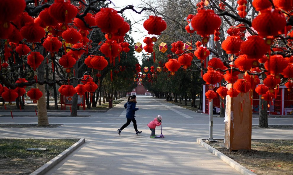 Una niña corre con un niño de pie en un scooter pasando linternas rojas antes del Año Nuevo Lunar Chino en un parque en Beijing | AFP/ Wang Zao