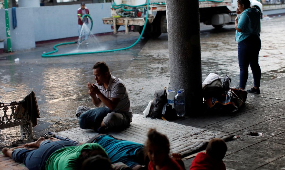 Un trabajador municipal riega la calle mientras los migrantes de América Central duermen en el suelo del parque central Miguel Hidalgo, México. / Reuters