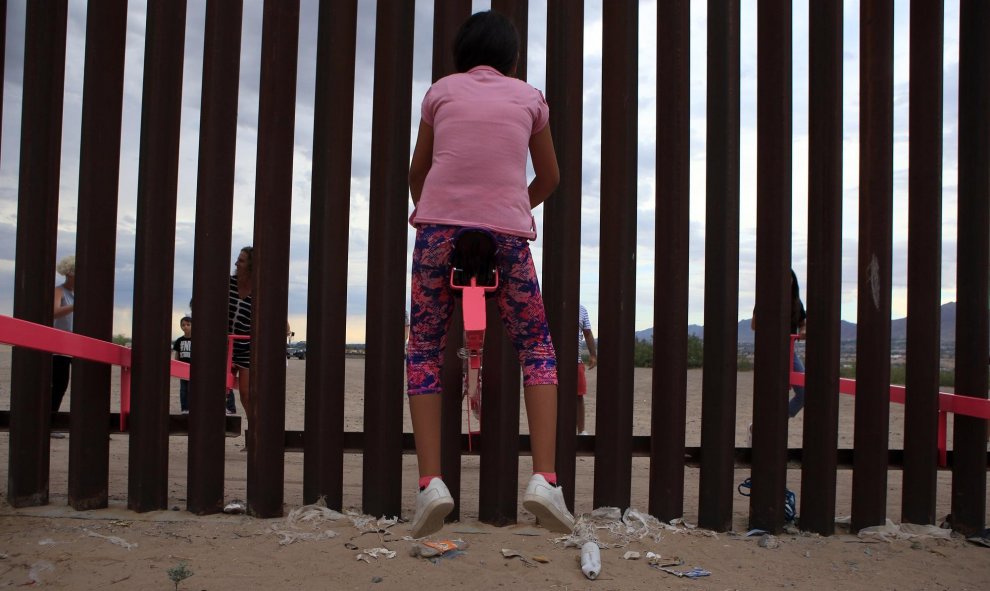 Una menor, vestida de rosa, se eleva en el aire mientras otro joven empuja el balancín desde el otro lado de la frontera. LUIS TORRES (AFP).