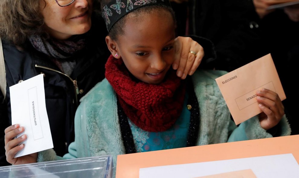 Una niña deposita el voto de una mujer en la urna. / Reuters.