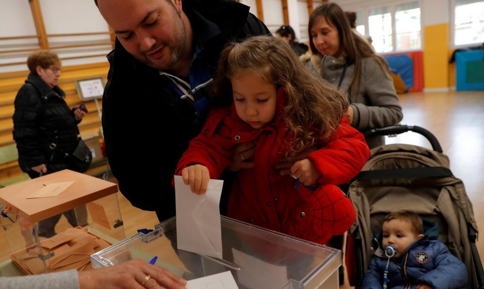 Una niña deposita el voto de su padre, que la sostiene en brazos. / Reuters