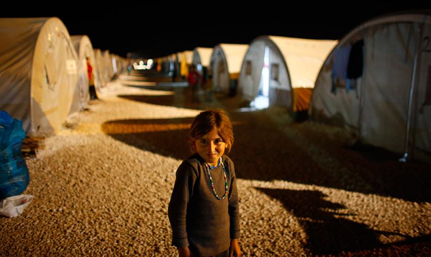 Una niña kurda sonríe a la cámara durante una noche en un campo de refugiados en la cuidad fronteriza de Suruc, provincia de Sanliurfa (Turkía). // OSMAN ORSAL (REUTERS)