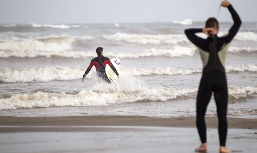 Dos jóvenes surfistas se disponen, esta tarde, a entrar en el mar a disfrutar de las olas que el temporal de Levante lleva hasta la orilla de la playa de Las Arenas de Valencia. El temporal de lluvias que afecta a la Comunitat Valenciana ha descargado pre