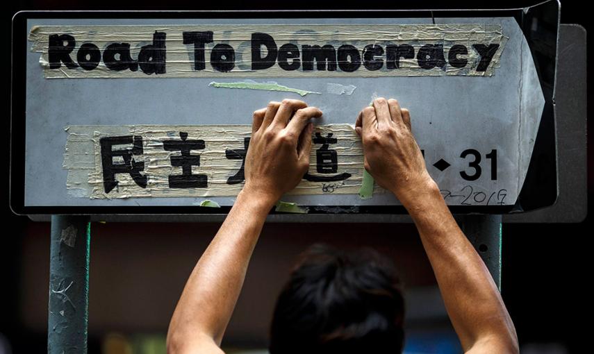 Un trabajador retira la cinta adhesiva de una señal en la que los manifestantes han escrito 'Camino a la democracia', durante el último 'Occupy' en Hong Kong. /ATHIT PERAWONGMETHA (REUTERS)