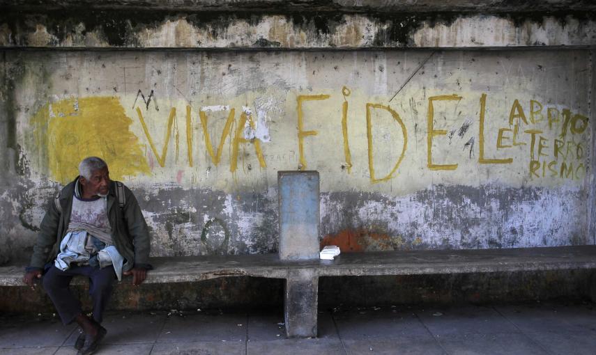 Un hombre sentado en un banco junto a una pintada que reza "Larga vida a Fidel". REUTERS/Stringer